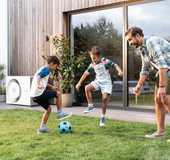 Family playing outside with heat pump shown in background