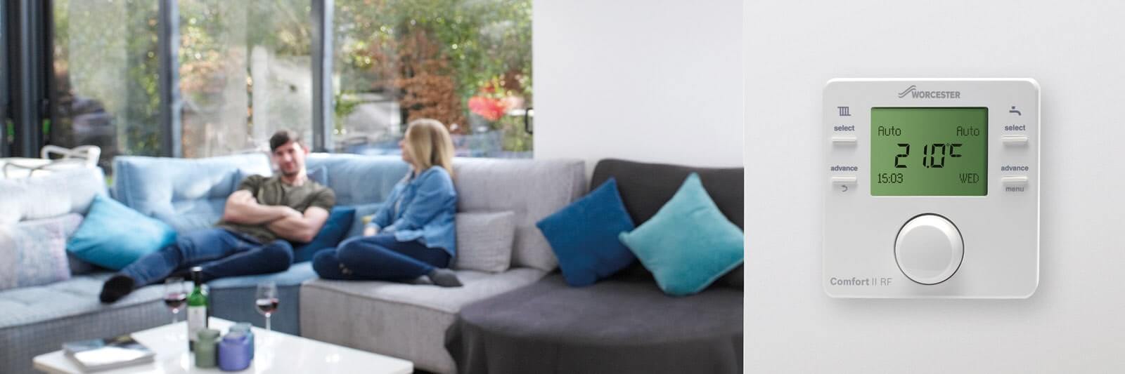 In focus boiler control panel on wall with man and woman on couch in the background.